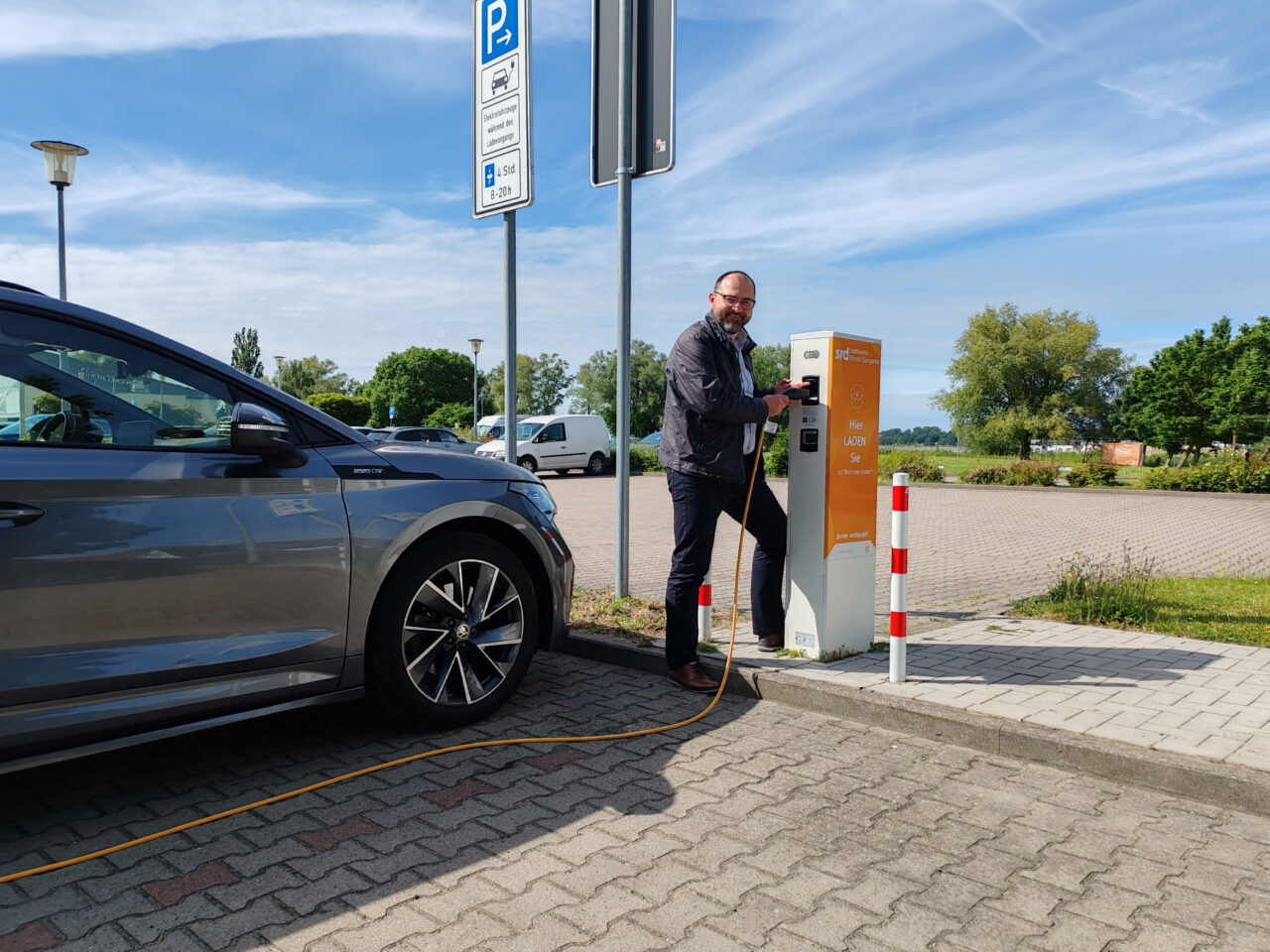 Bild zeigt den Geschäftführer Sebastian Pott an der Ladesäule Boddentherme, wie er sein E-Auto mit orangem Kabel läd.